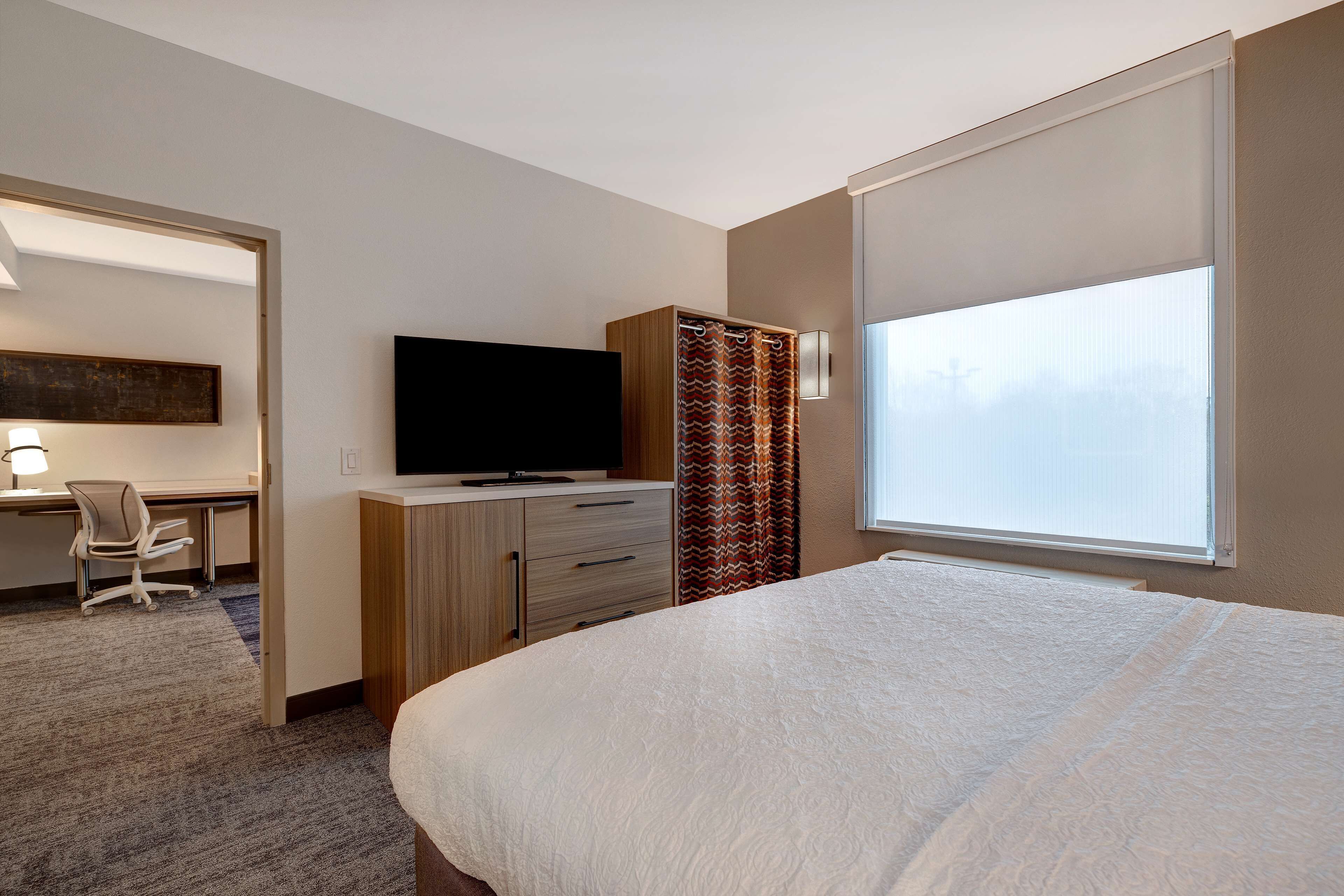 Ein Hotelzimmer mit einem Bett, einem Schreibtisch mit Stuhl, einem Fernseher und einem Fenster mit Vorhängen.