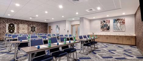 A conference room with multiple tables and chairs, equipped with water bottles, and decorated with abstract wall art.