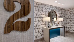 A modern hotel lobby with a large wooden number '2' sign, a geometric patterned wall, and a blue accent in the reception desk area.