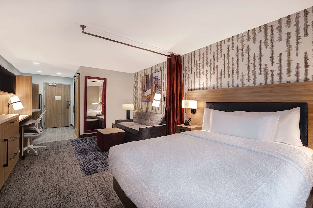 Une chambre d’hôtel avec un grand lit, un bureau avec une chaise, un petit canapé, une télévision et une tête de lit en bois.