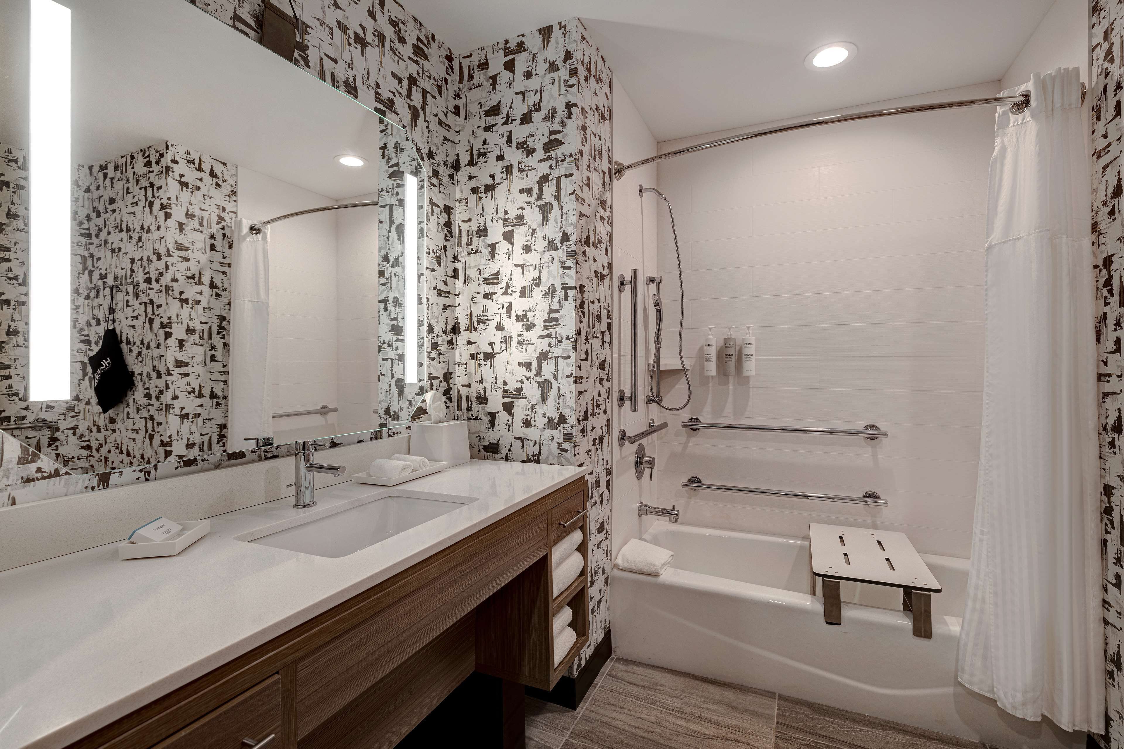 A modern bathroom with a large mirror, two sinks, a bathtub, and a shower.