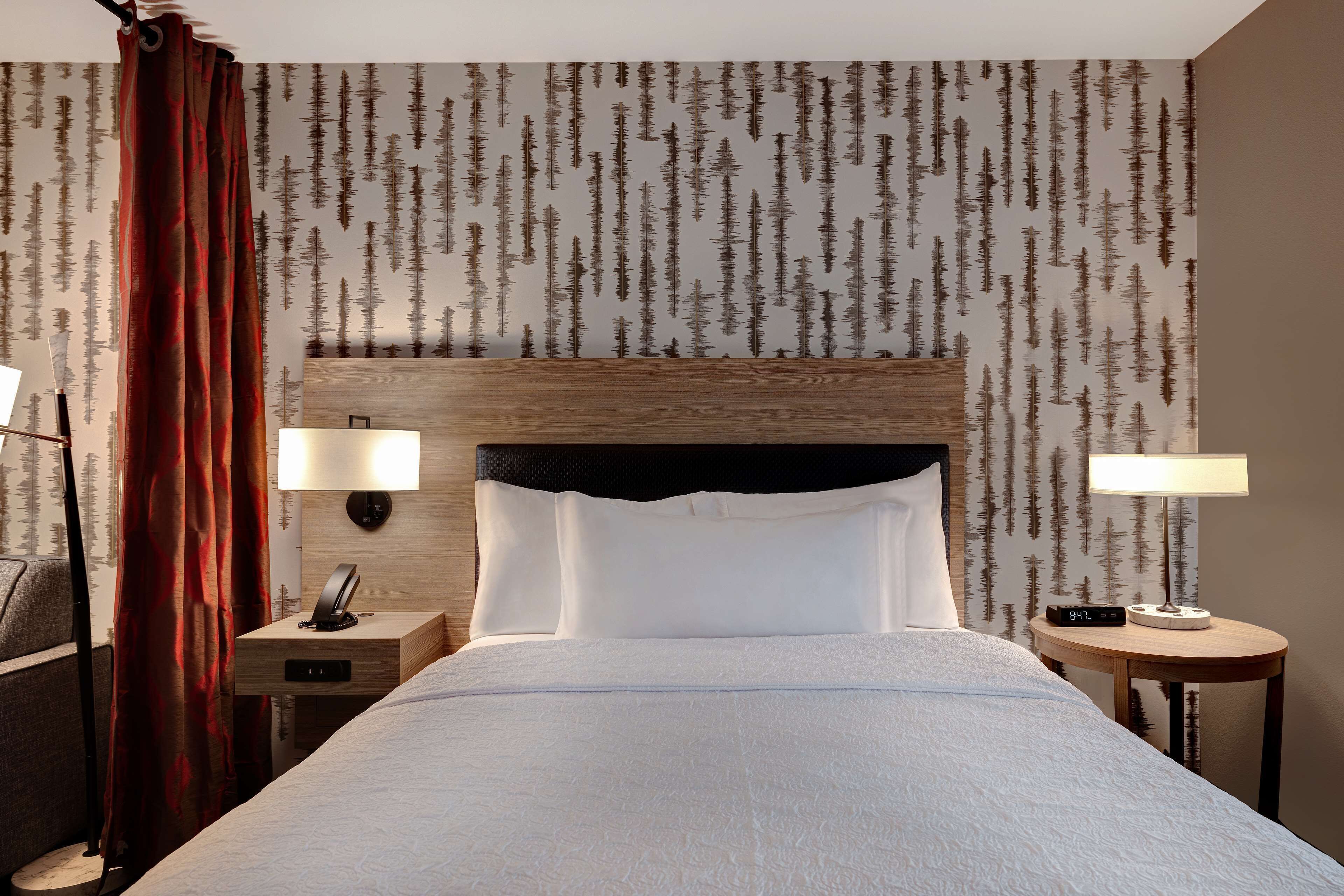 Habitación de hotel con una cama, dos mesitas de noche con lámparas, un cabecero y una cortina.