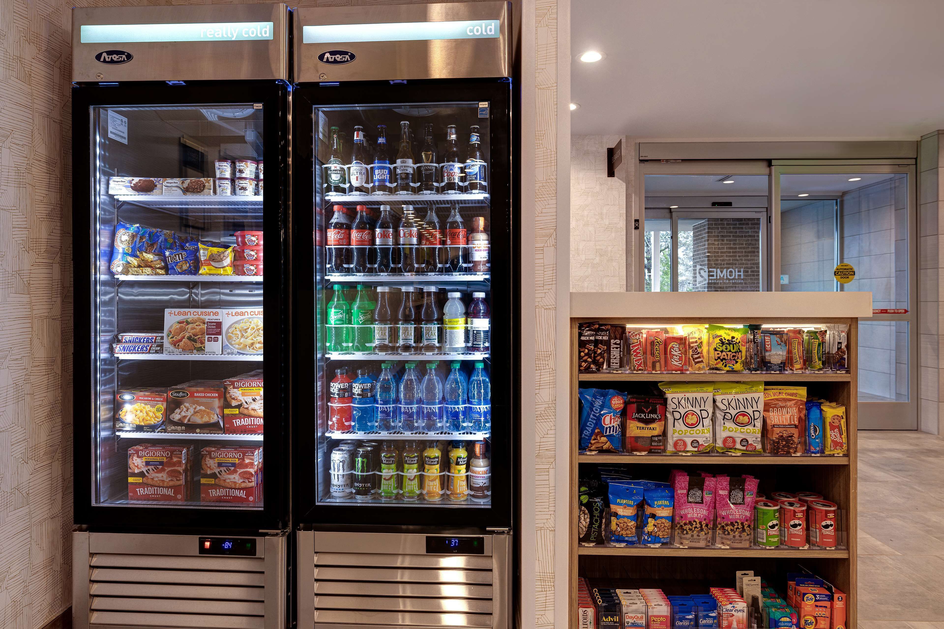 Twee gekoelde drankdispensers gevuld met verschillende dranken en snacks, en een plank met diverse houdbare producten.