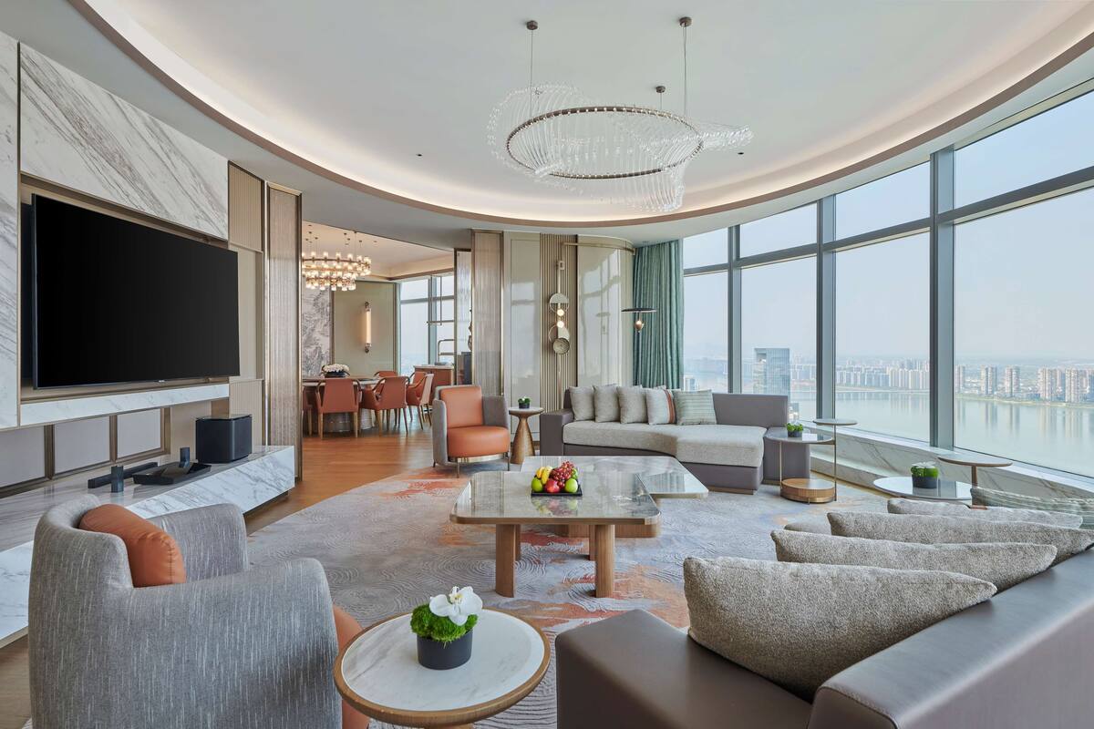 A modern living room with a large TV, comfortable seating, a coffee table, and a view of the city.
