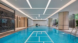 An indoor swimming pool with a clear waterline, geometric ceiling design, and a view of the outdoors through a glass wall. - Hilton Changsha Riverside (Changsha)