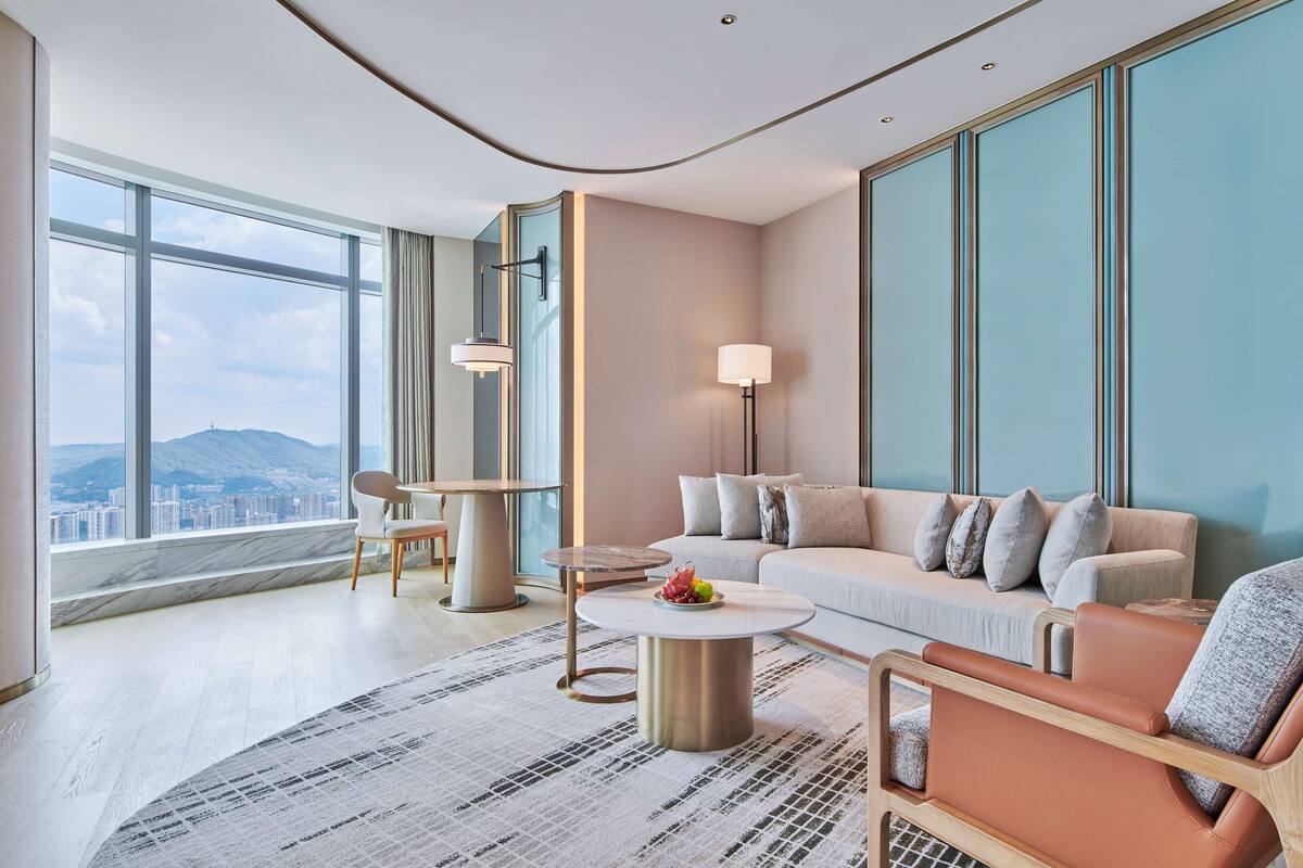 A modern living room with a large window, a sofa, a coffee table, and a dining area.