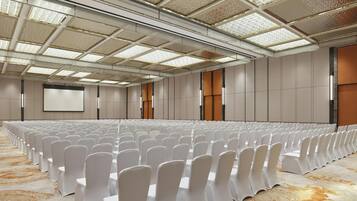 Ein Konferenzraum mit Reihen weißer Stühle, einem großen Bildschirm und einem gemusterten Teppich.