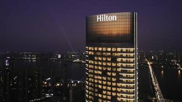 Ein Hochhaus mit dem Hilton-Logo, das ein modernes architektonisches Design mit einer auffälligen Glasfassade und beleuchteten Fenstern aufweist.