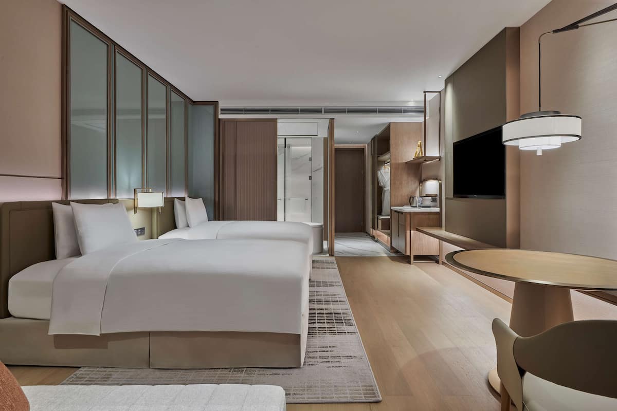 A modern hotel room with a large bed, a desk, a TV, and a wardrobe.