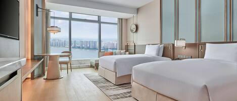 A modern hotel room with two beds, a desk, and a large window offering a city view.