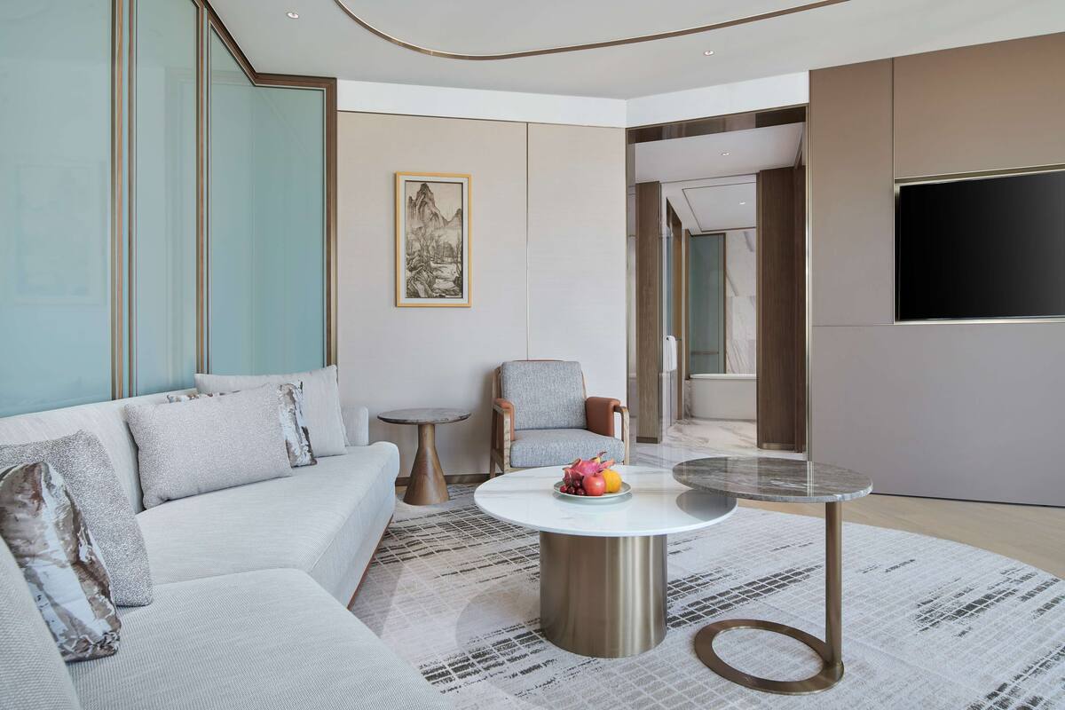 A modern living room with a sofa, a round coffee table with fruit, a chair, and a TV mounted on the wall.
