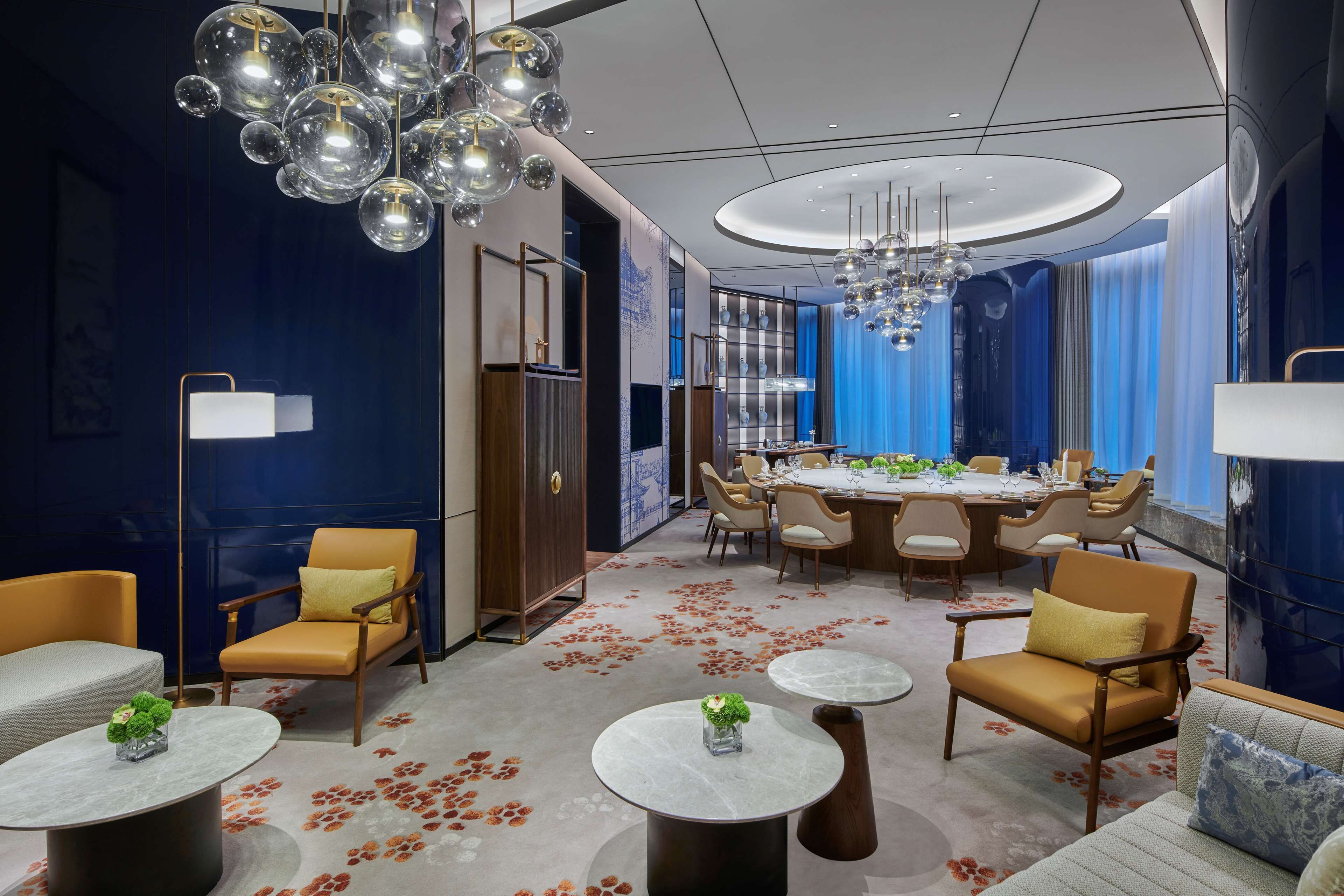 A modern hotel lobby with a round dining table, comfortable seating, and decorative lighting.