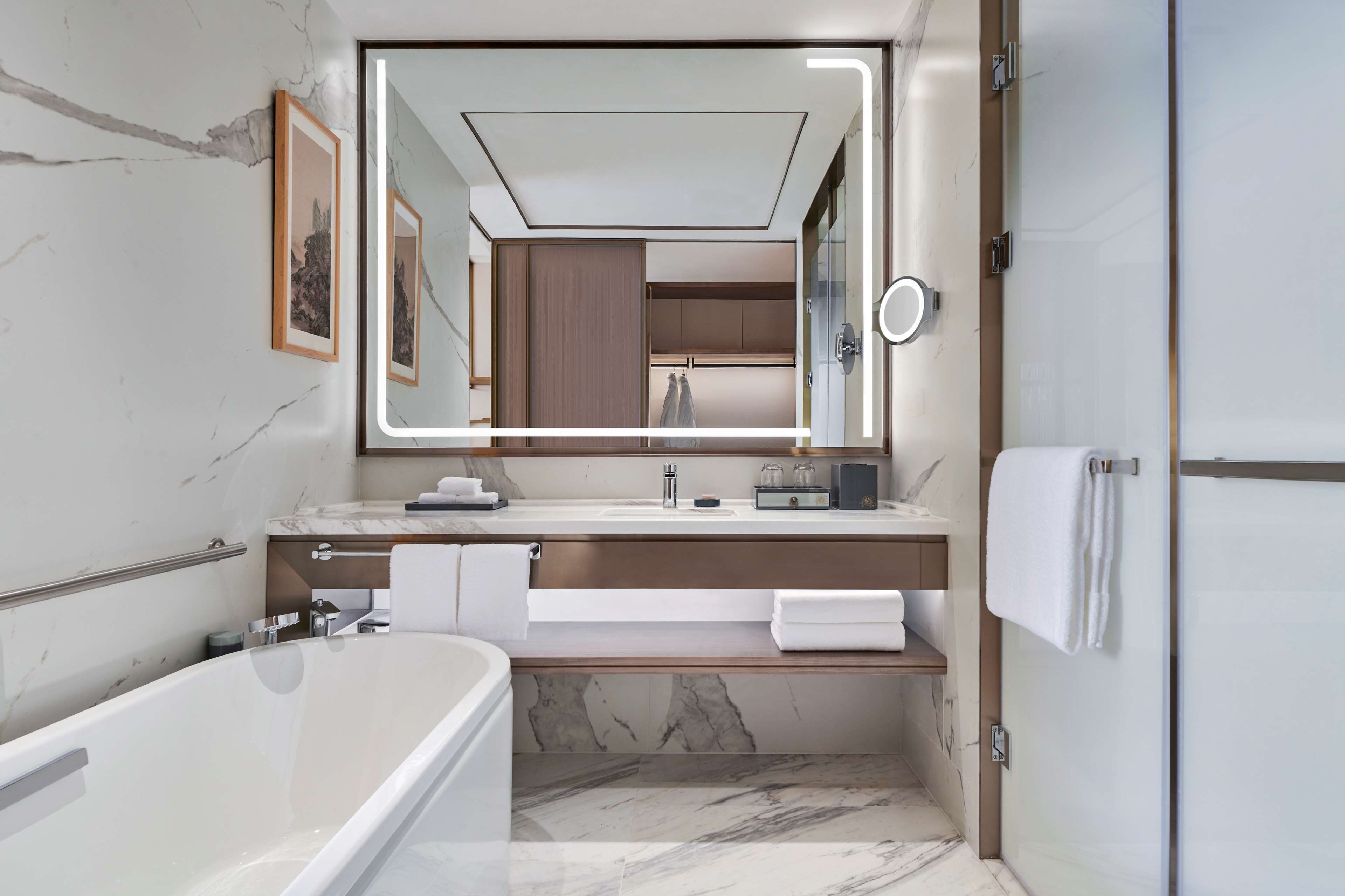 A modern bathroom with a large mirror, marble walls, a bathtub, and a shower area.