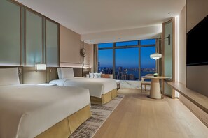 A hotel room with two beds, a desk, a chair, a TV, and a large window with a city view.