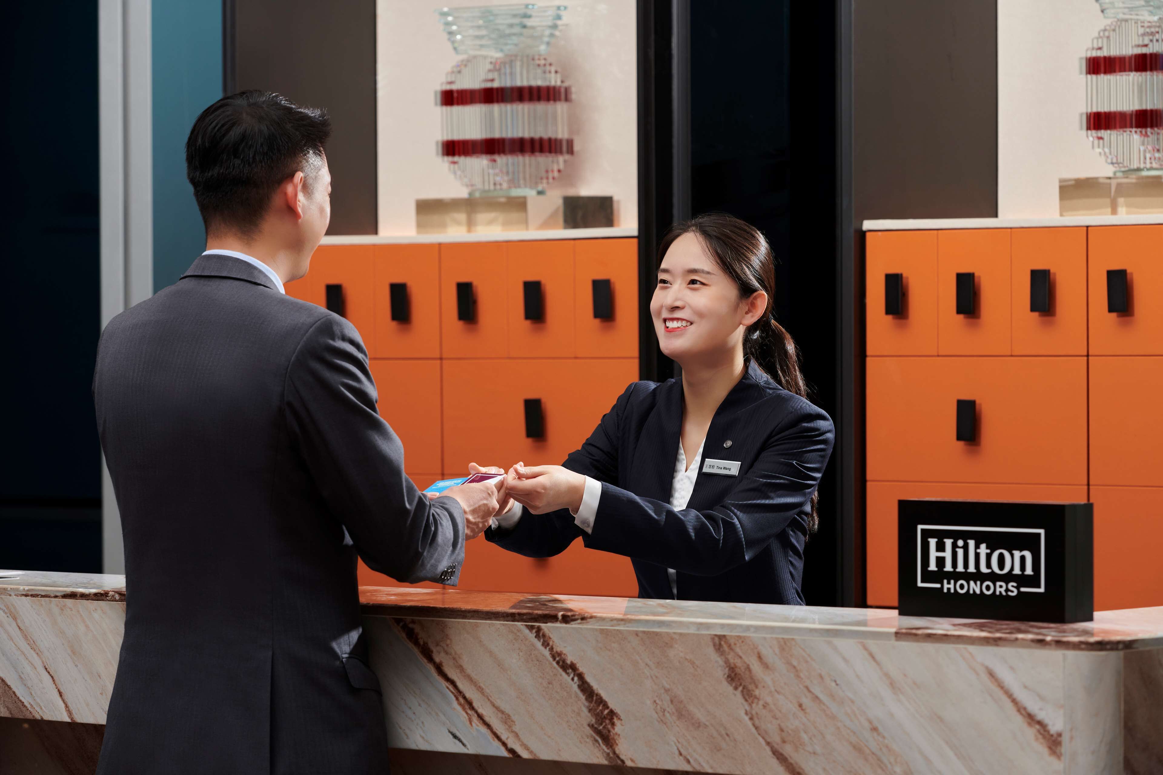 A hotel reception desk with a marble counter, a name tag, and a sign indicating 'Hilton Honors'.