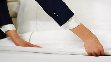 A hand adjusting a white bedspread on a bed with a white pillow.