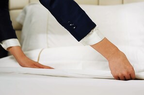 A hand adjusting a white bedspread on a bed with a white pillow. - Hilton Changsha Riverside (Changsha)