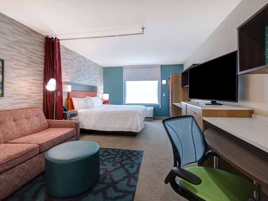 A hotel room with a bed, a sofa, a desk with a chair, a TV, and a window with curtains.