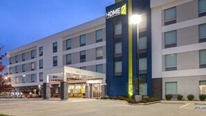 Un hôtel moderne, reconnaissable à son grand panneau « HOME 2 », qui s’étend sur plusieurs étages et possède un hall d’entrée abrité.