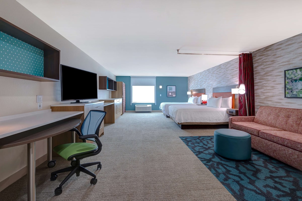 A hotel room with a desk, chair, television, bed, and a sofa.