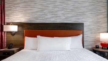 A hotel room with a large bed, two bedside tables, a nightstand, a red lamp, and a wall-mounted lamp.