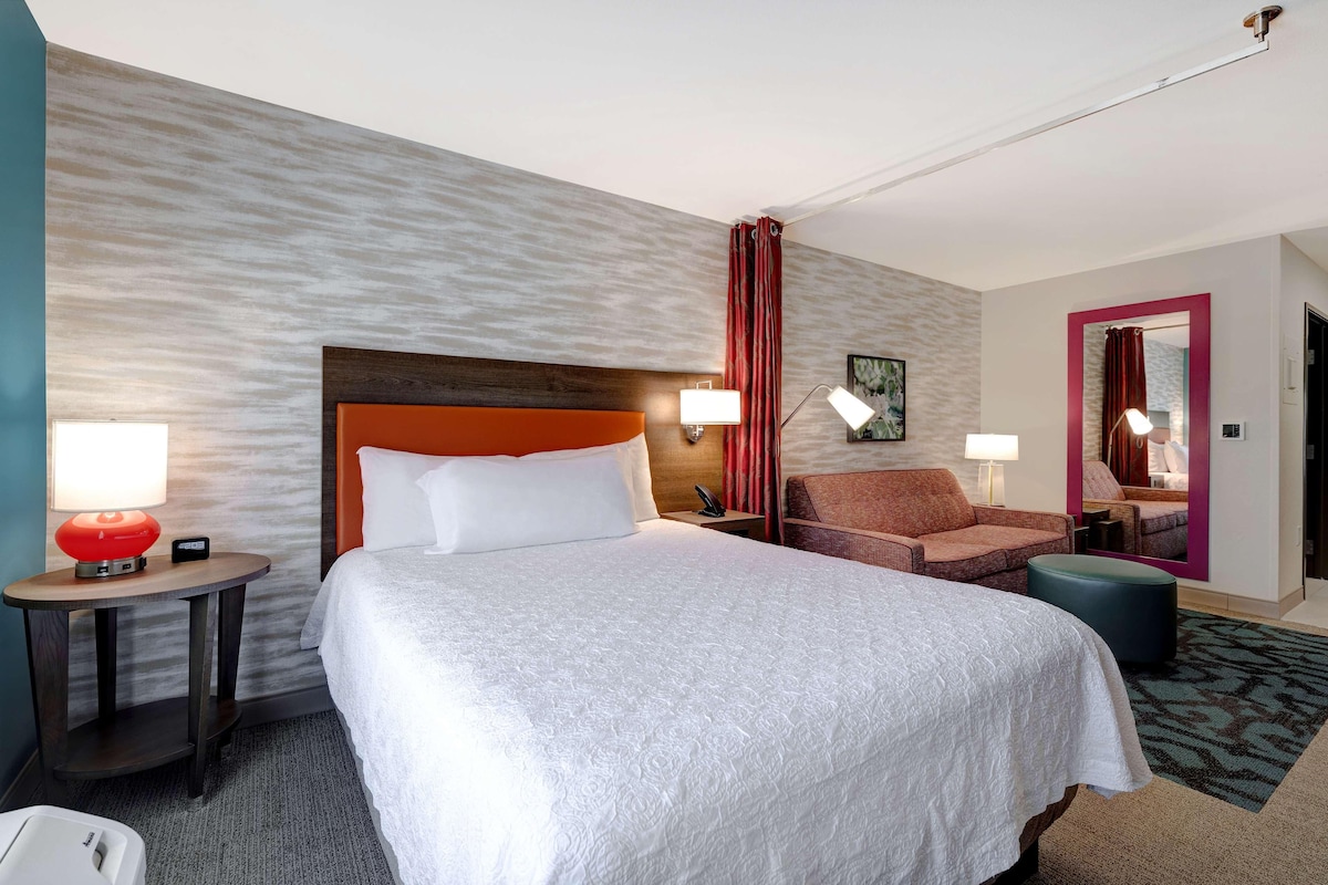 Una camera d'albergo con un letto grande, un divano, un tavolino rotondo e uno specchio.