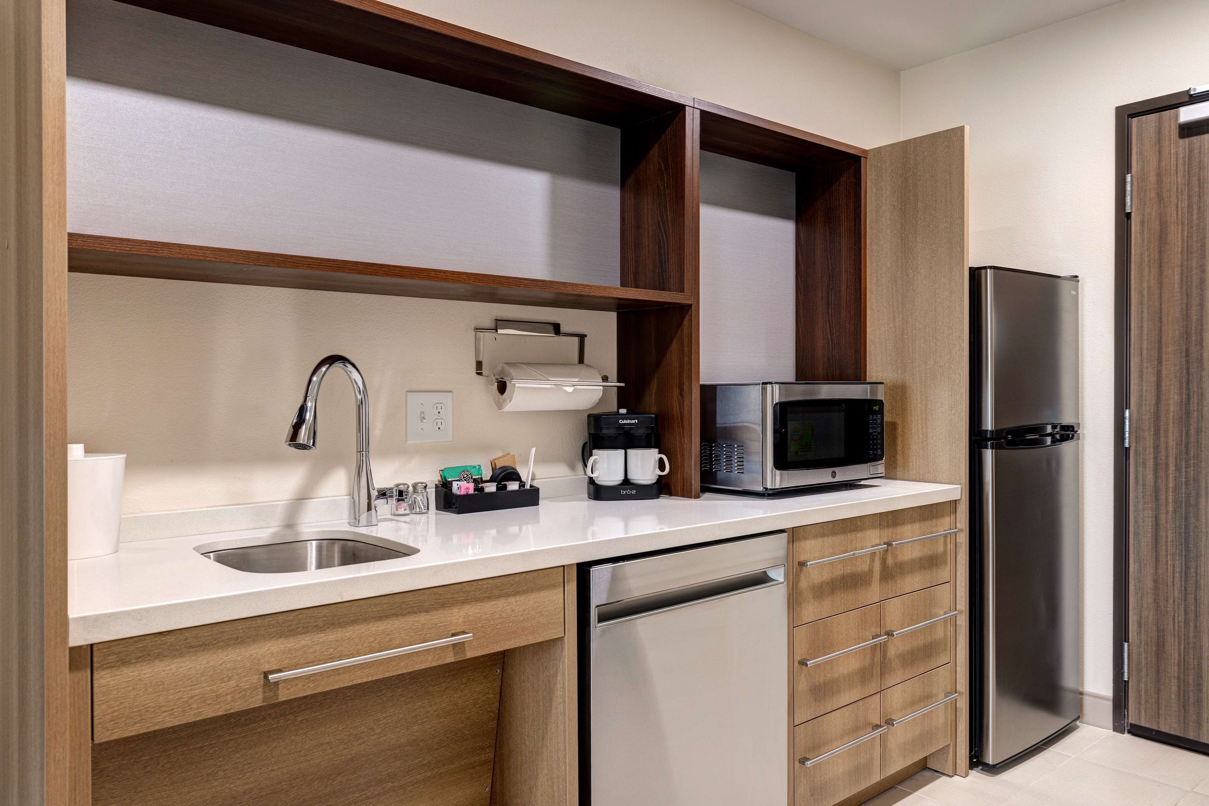 Una cocina moderna con un lavamanos de acero inoxidable, una cafetera, un microondas y un refrigerador.
