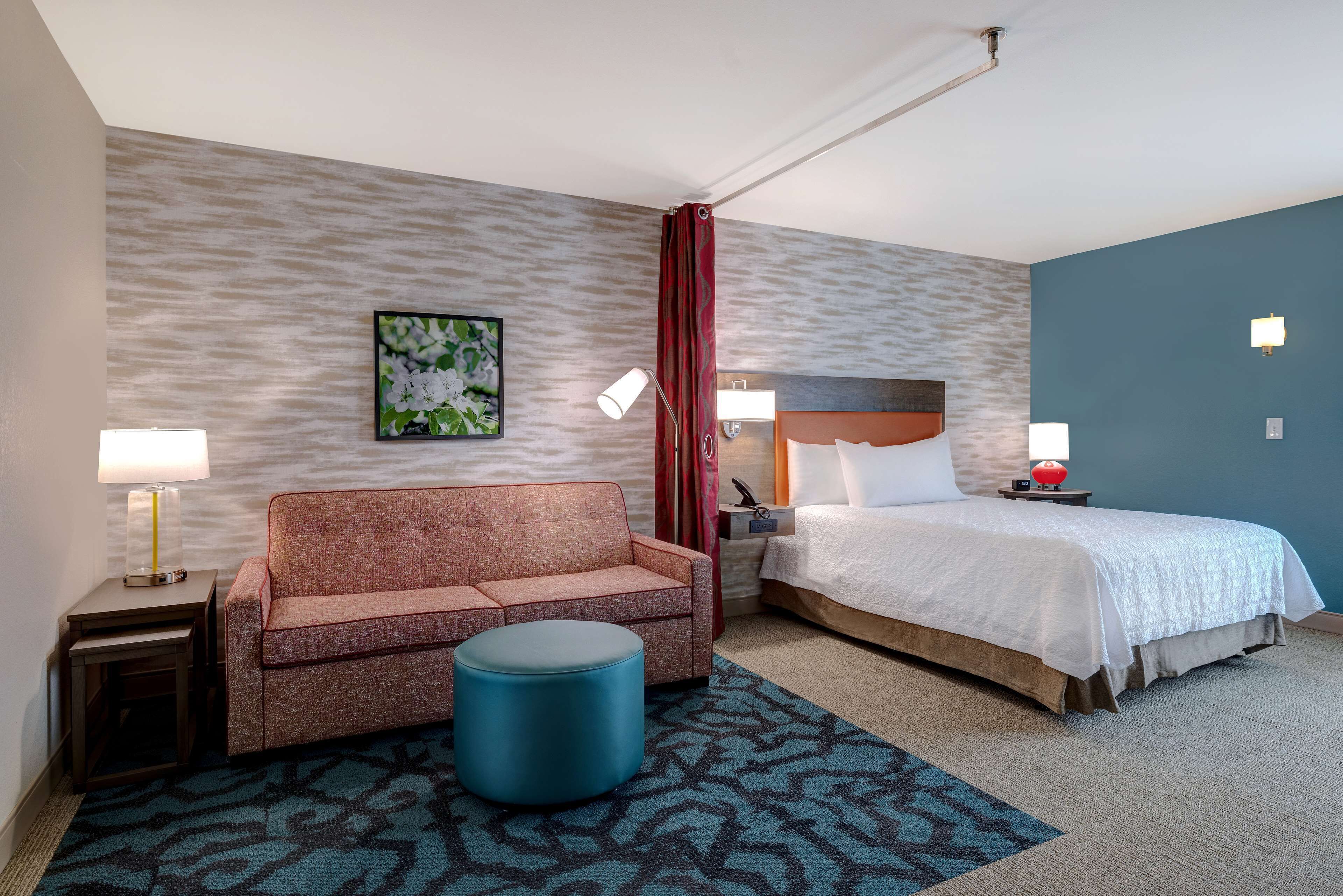 A hotel room with a bed, a sofa, a small table, a lamp, and a decorative wall piece.