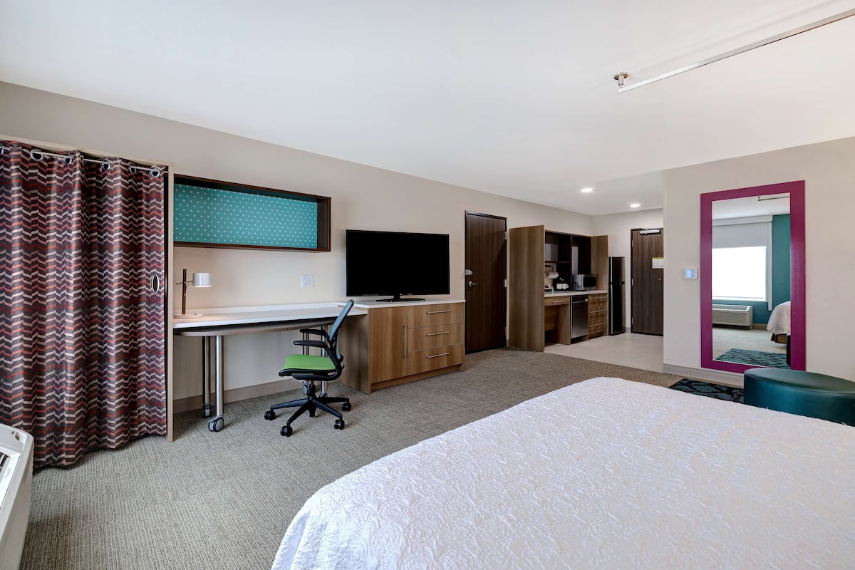 A hotel room with a bed, desk, chair, TV, wardrobe, and bathroom.