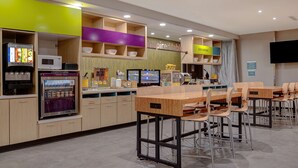 Un restaurant moderne doté d’un espace de libre-service pour les boissons, d’un menu numérique affiché sur écran et d’une salle à manger conviviale avec des tables et des chaises en bois.