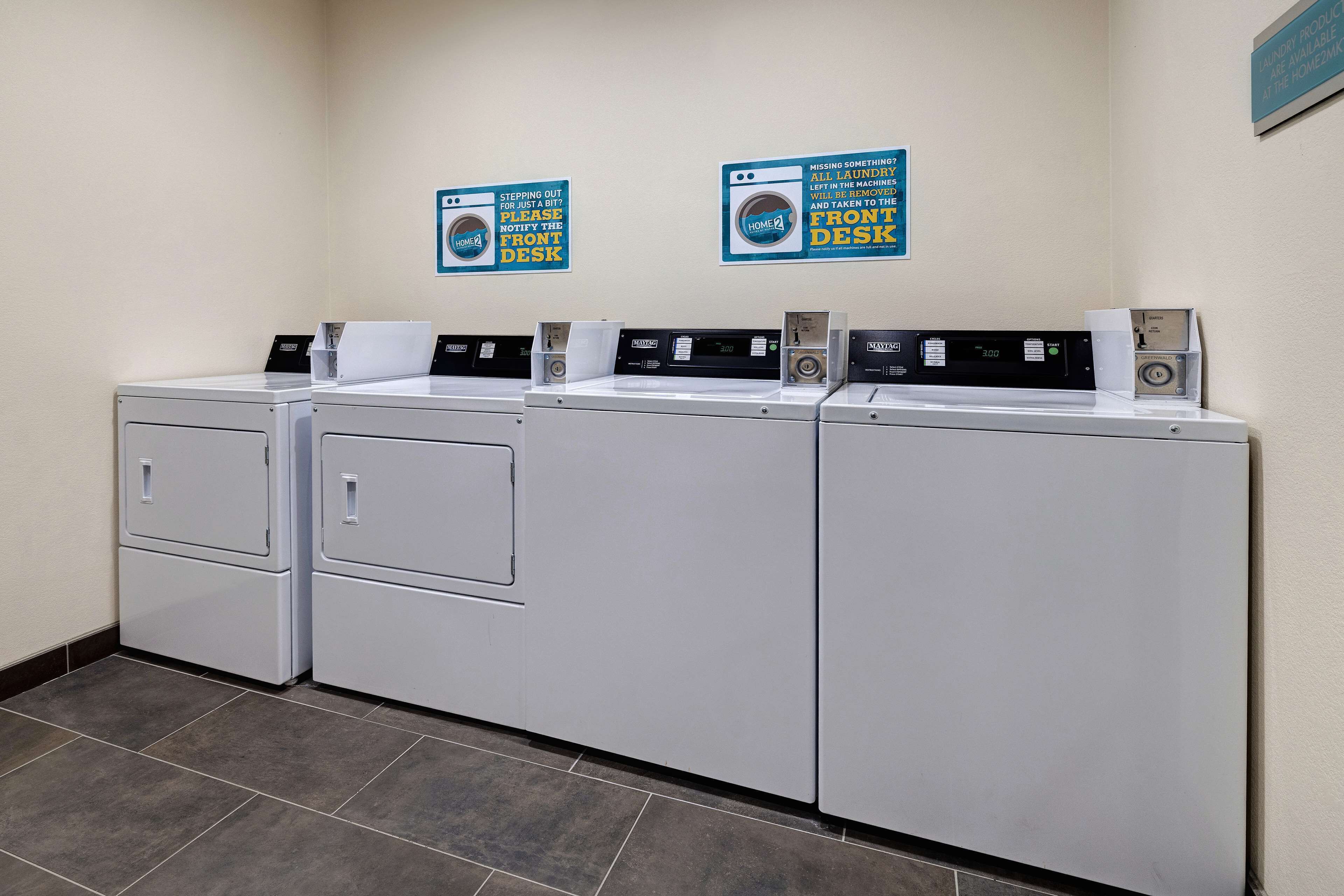 A laundry facility with four washing machines and two signs on the wall.