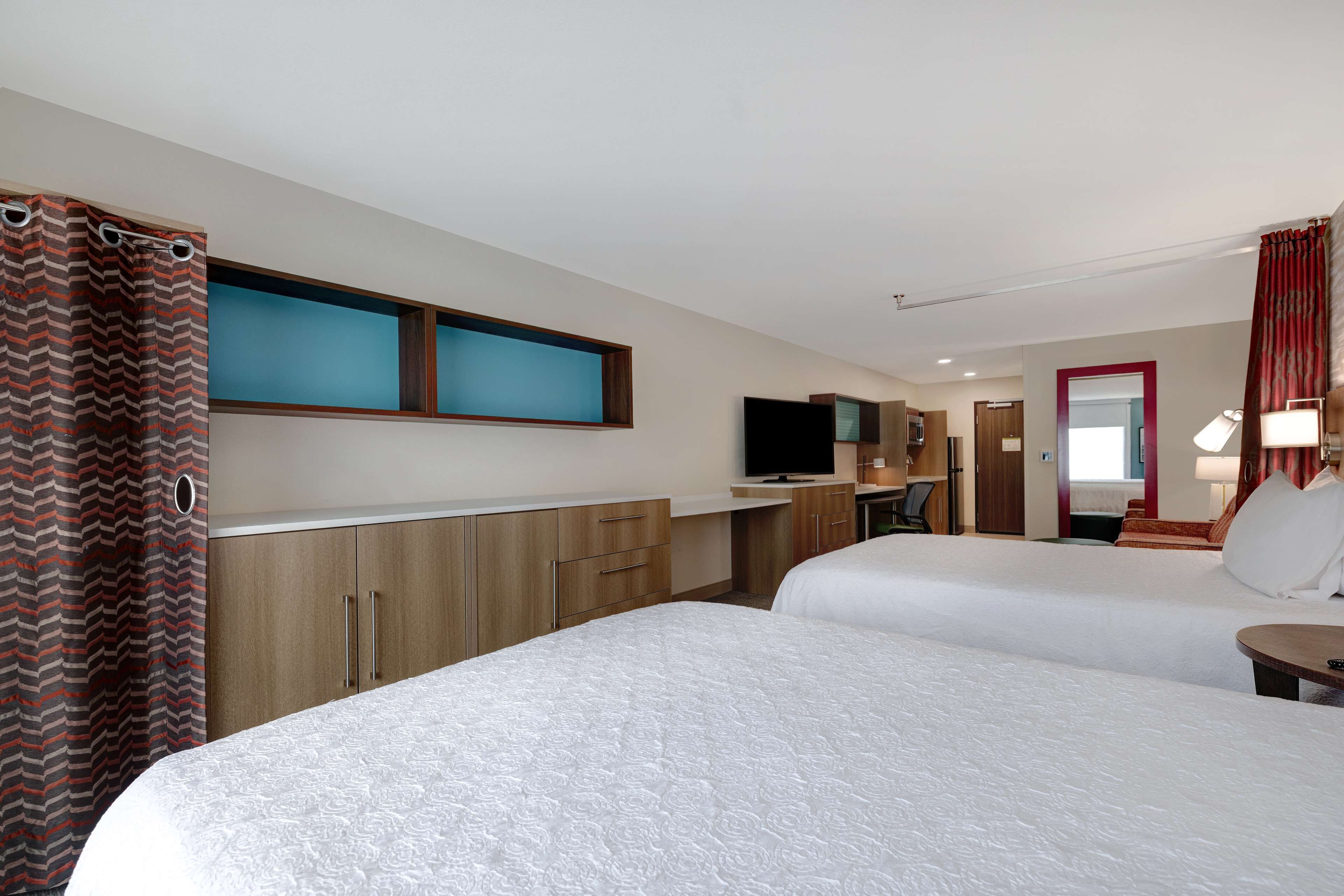 A hotel room with two beds, a TV, a desk, and a bathroom visible through an open door.