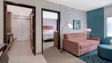Habitación de hotel con cama, sofá, escritorio y baño visible a través de una puerta abierta.