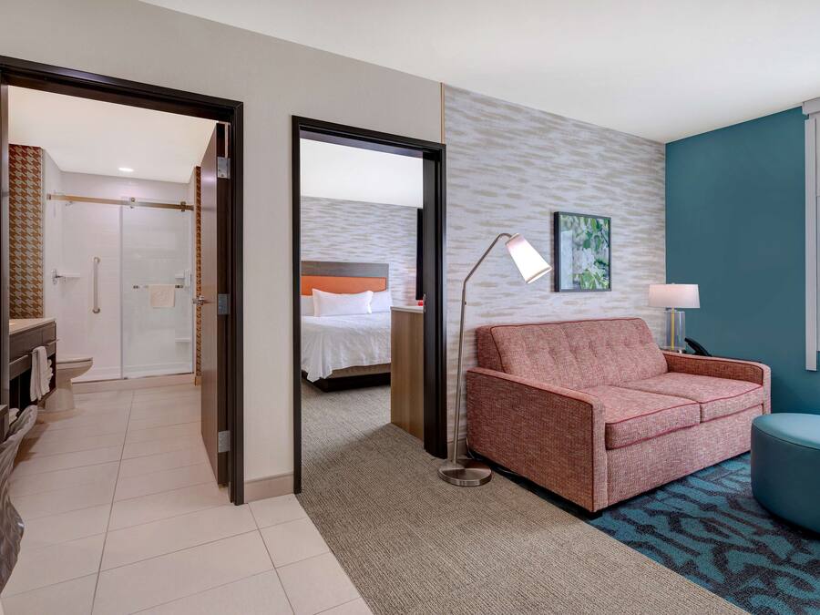 Habitación de hotel con cama, sofá, escritorio y baño visible a través de una puerta abierta.