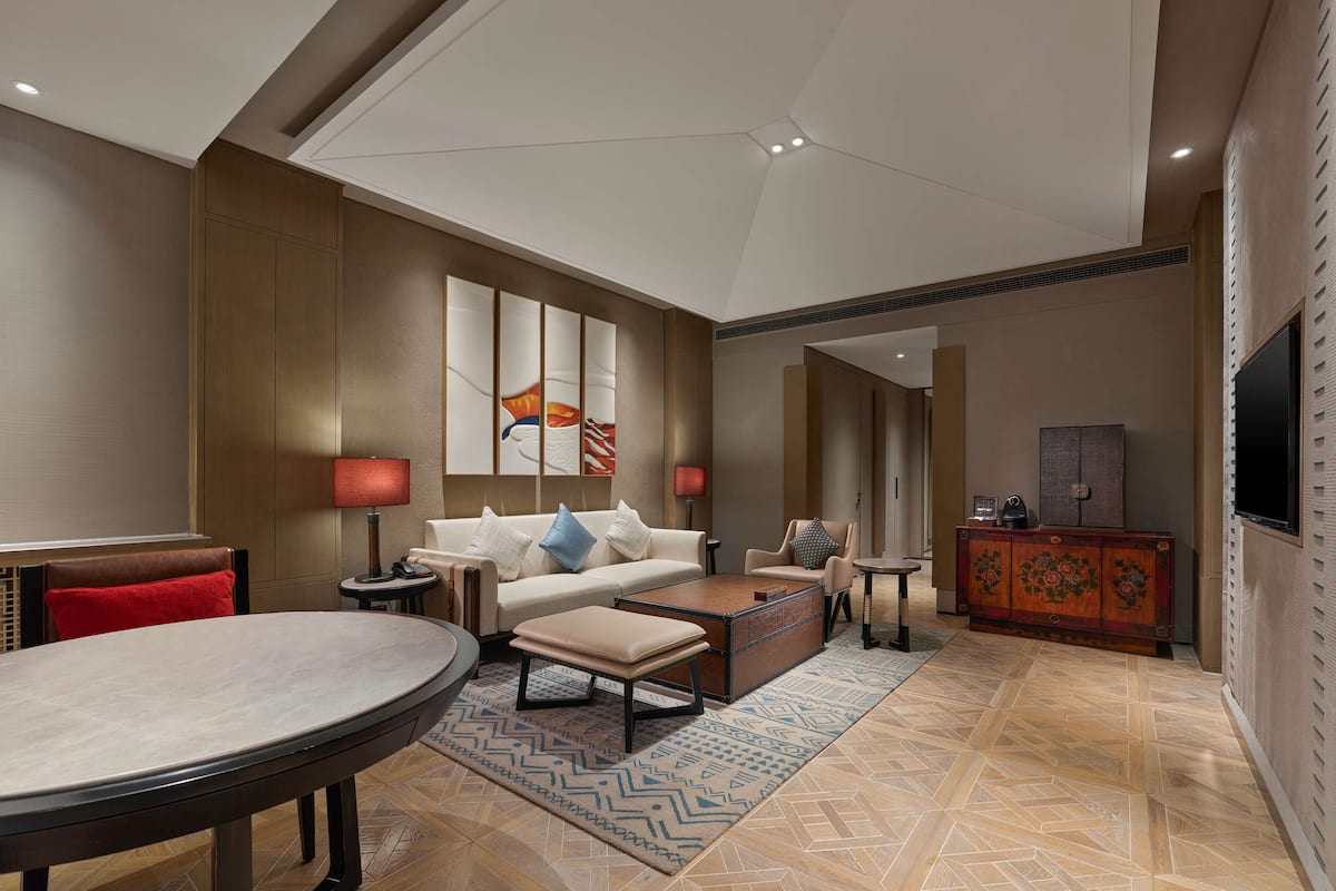 A spacious living area with a high ceiling, a large painting, a sofa, a coffee table, a TV, and a decorative cabinet.