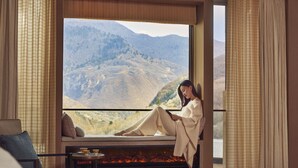 A room with a large window offering a mountain view, a sofa, a small table with a cup, and a fireplace. - Conrad Jiuzhaigou (Ngawa Autonomous Prefecture)