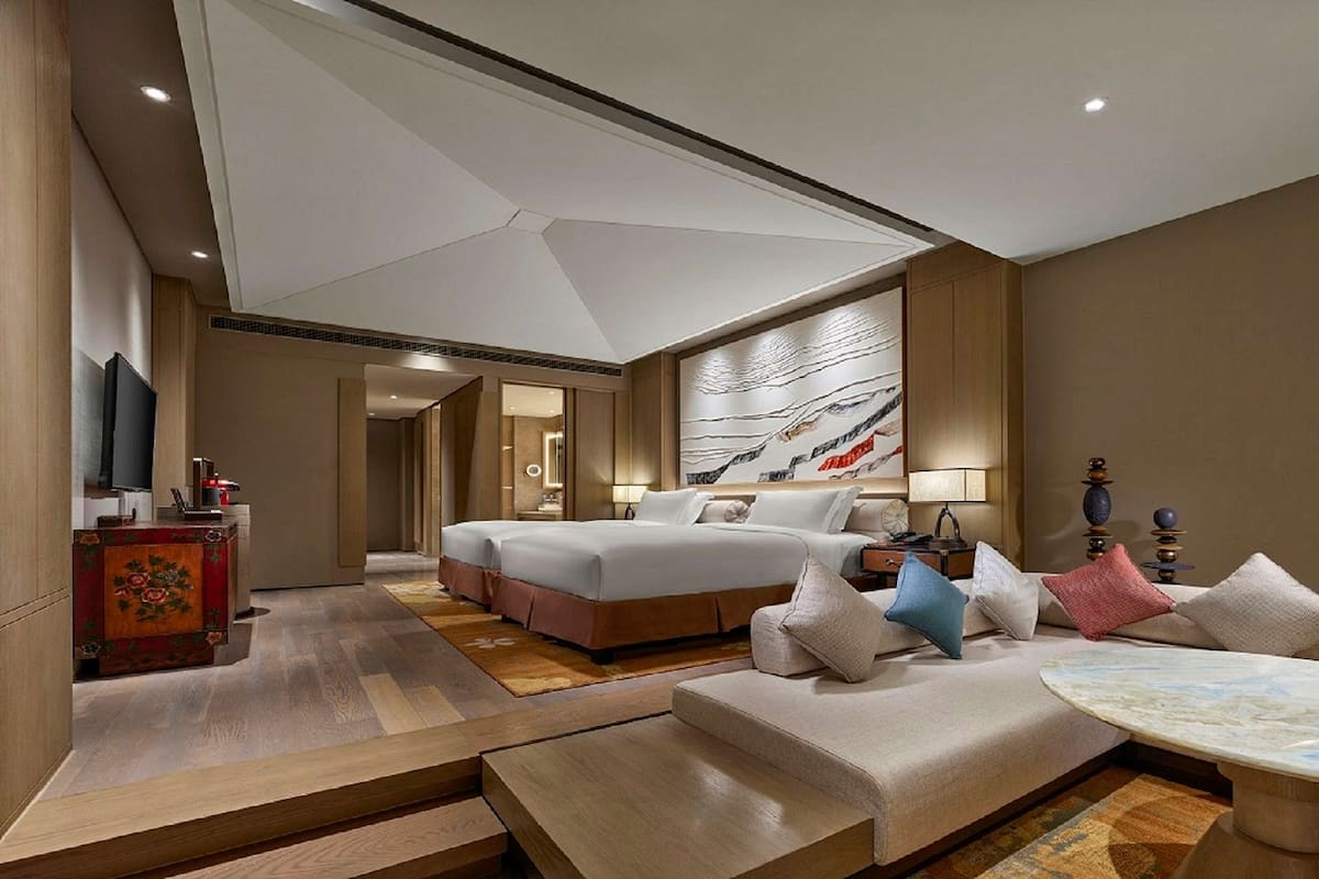 A modern hotel room with a large bed, a sofa, a coffee table, and a TV.