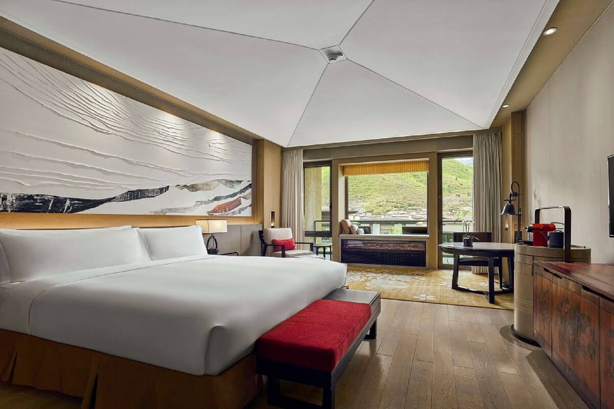 A hotel room with a large bed, a desk, a television, and a view of the outdoors.