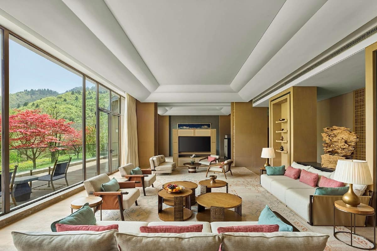 A spacious living room with a large TV, comfortable seating, and a view of a lush garden.