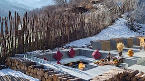 A cozy outdoor seating area with a fire pit, logs, and a view of snow-covered mountains. - Conrad Jiuzhaigou (Ngawa Autonomous Prefecture)