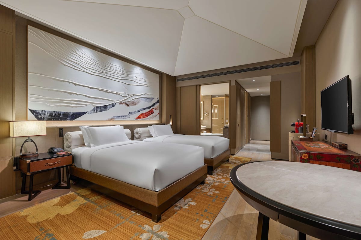 A hotel room with two beds, a large wall art piece, a flat-screen TV, and a small table.