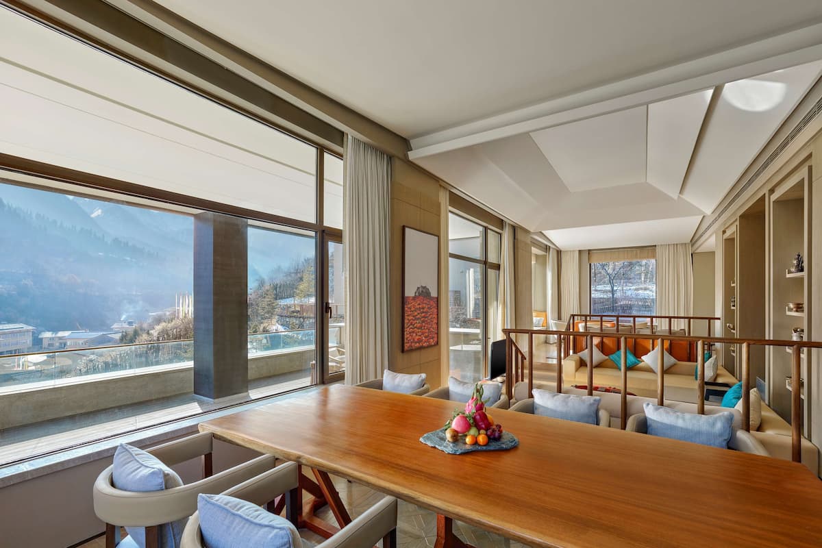 A spacious room with a large wooden table, comfortable seating, and a view of a mountainous landscape through large windows.