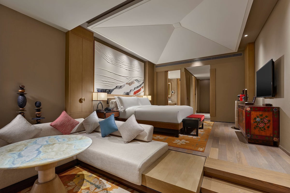 A hotel room with a bed, a sofa, a table, a TV, and a decorative wall piece.
