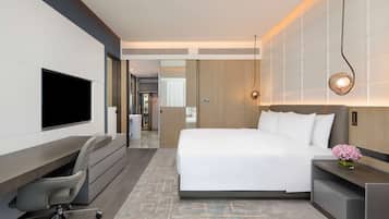 Ein modernes Hotelzimmer mit Bett, Schreibtisch, Stuhl, Fernseher und einem kleinen Tisch mit Blumen.