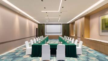 A conference room with a long table, white chairs, and a projector screen.