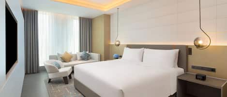 Une chambre d’hôtel moderne dotée d’un grand lit, d’un coin salon avec un canapé et un fauteuil, d’une télévision à écran plat et d’une table de chevet avec une lampe.