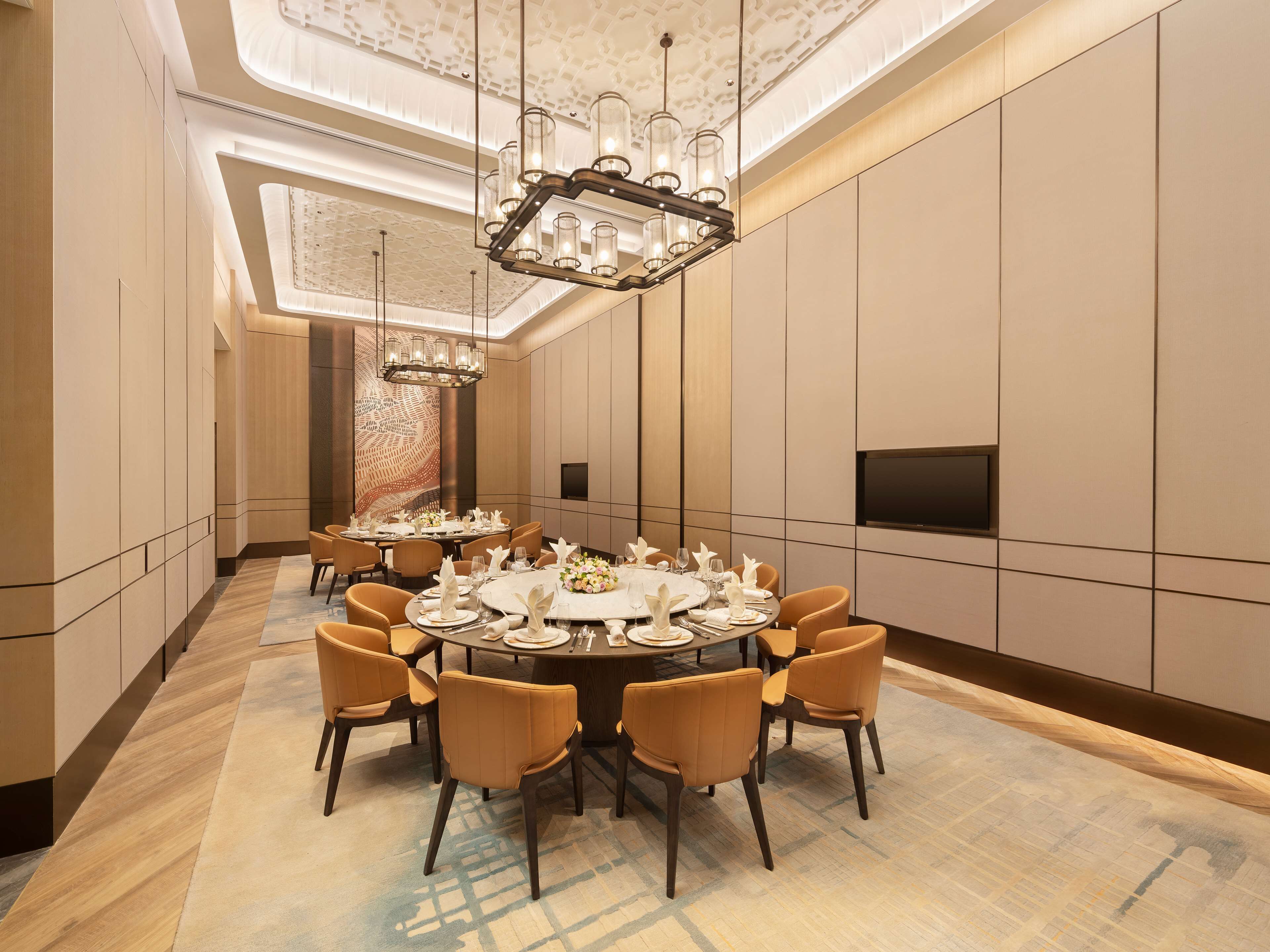A spacious dining area with a round table set for a meal, surrounded by chairs, and a modern chandelier above.