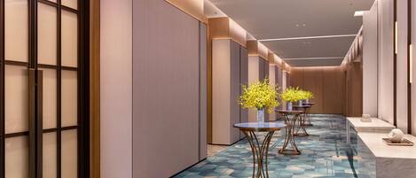 Een moderne hotelgang met een kamerbreed tapijt, inbouwverlichting en decoratieve vazen met gele bloemen.