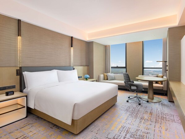 Habitación de hotel con una cama grande, un sofá, un escritorio y vistas a la ciudad.