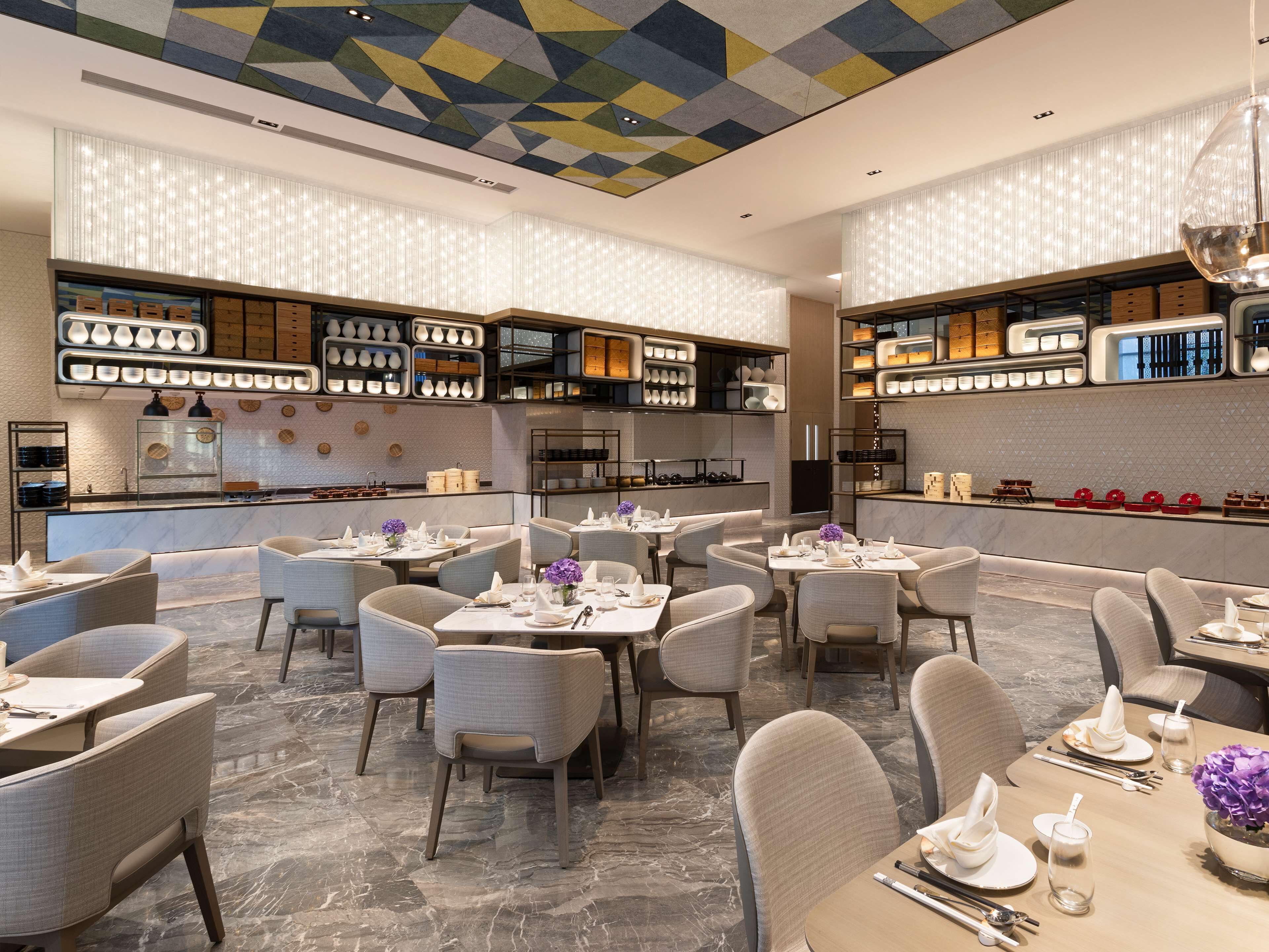 Ein modernes Restaurant mit Marmorböden, ordentlich aufgestellten Tischen und Stühlen sowie einem geometrischen Deckenmuster.